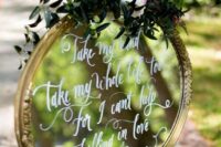 a mirror in a gold frame, with greenery and blooms plus a white calligraphy quote is a lovely decoration for a wedding