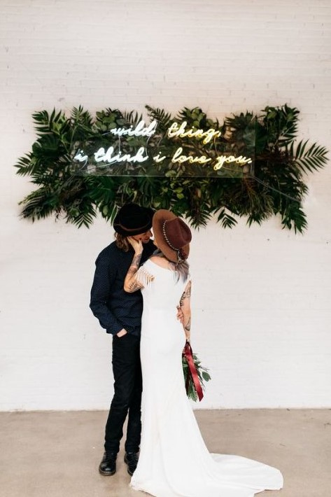 a modern boho wedding backdrop with tropical leaves and a neon sign is a fun idea