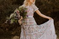a neutral A-line wedding dress with colorful floral embroidery all over and short sleeves plus a floral crown