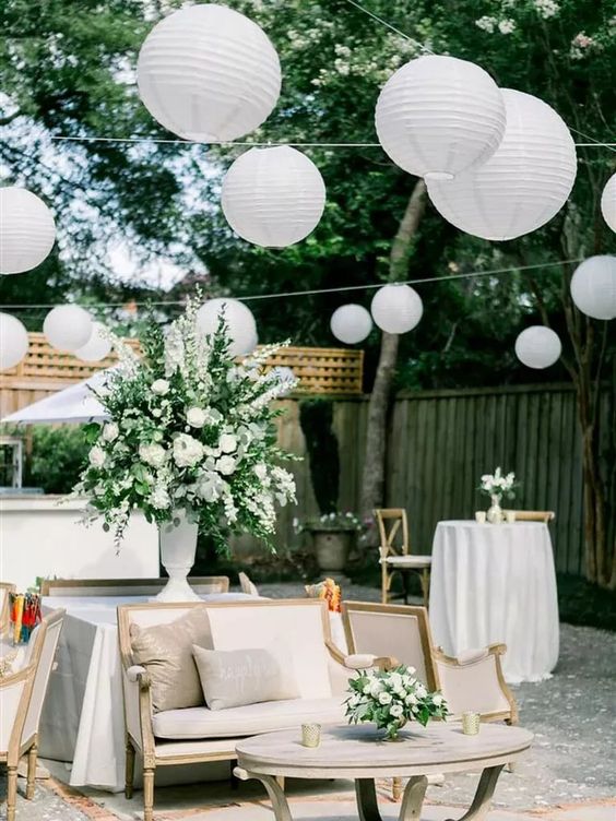 a neutral outdoor wedding lounge with white paper lanterns, white and green floral arrangements and chic vintage furniture
