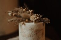 a neutral textural wedding cake with a quote topped with dried grasses and berries is a cool idea for a boho wedding