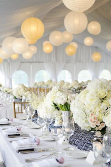 a neutral wedding reception space with a navy and white patterned table runner, white blooms on the tables and neutral paper lanterns