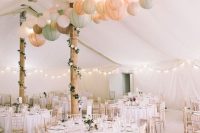 a neutral wedding reception space with greenery garlands, pastel paper lanterns and usual string lights is very welcoming