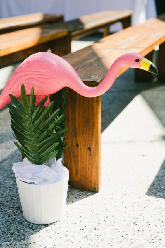 a planter with tropical leaves and a pink flamingo is a fun idea to line up the aisle and make it cooler