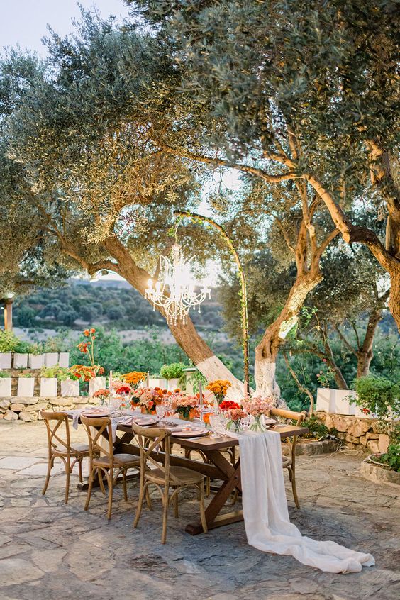 a pretty small outdoor wedding reception under the trees, with bright florals and a glam crystal chandelier hanging over the table