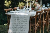 a refined wedding table setting with a white fabric runner and quotes, delicate blooms and greenery and white candles