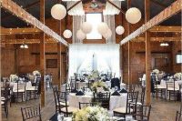 a rustic barn wedding reception decorated with neutral fabric, white paper lanterns, neutral tablescapes and navy napkins is wow