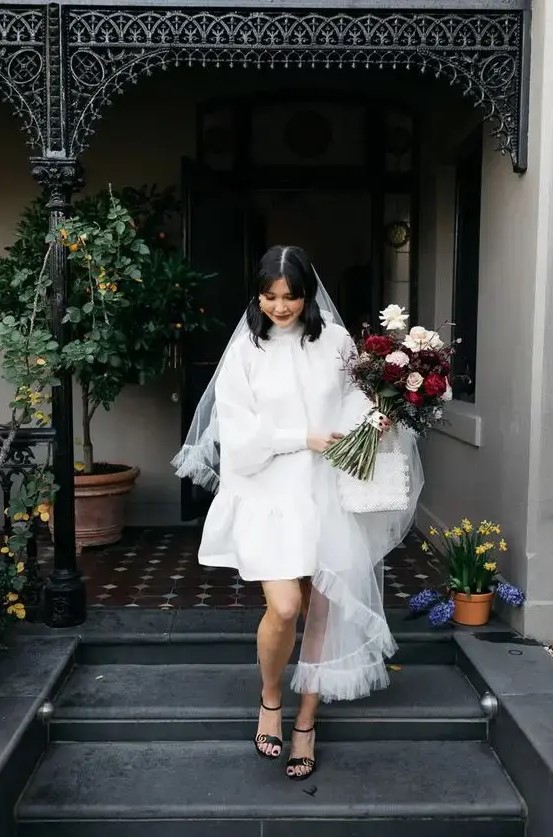 a short A-line wedding dress with a turtleneck and puff sleeves, black heels and a veil for a retro look