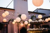a stylish and chic outdoor wedding reception space with paper lanterns and string lights, with a lit up fountain is amazing