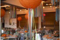 a super bright wedding reception space with printed tablecloths and bright blooms, orange napkins and orange paper lanterns with ribbon