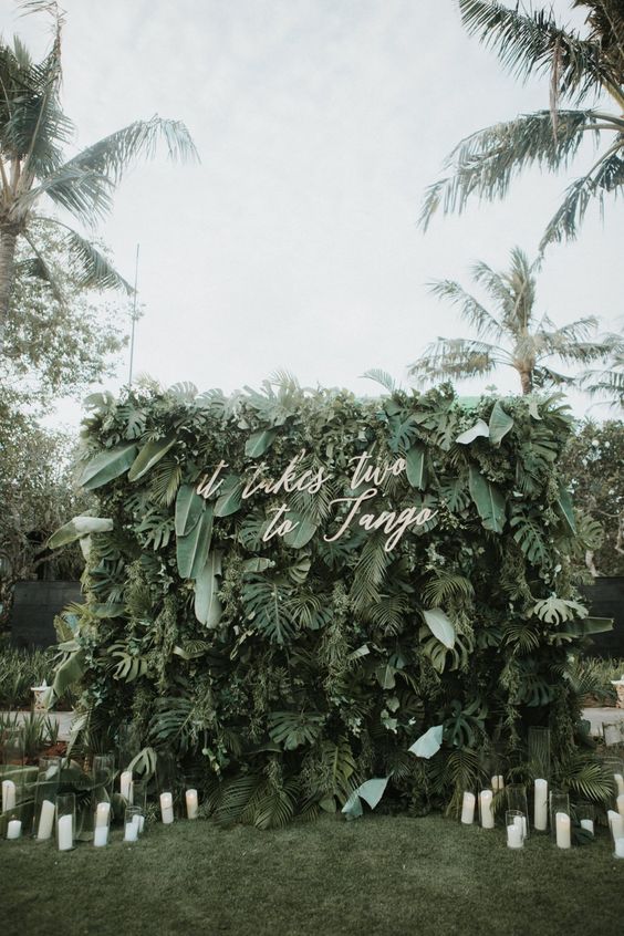a super lush tropical leaf wall with calligraphy and candles around is a lovely modern wedding idea to rock