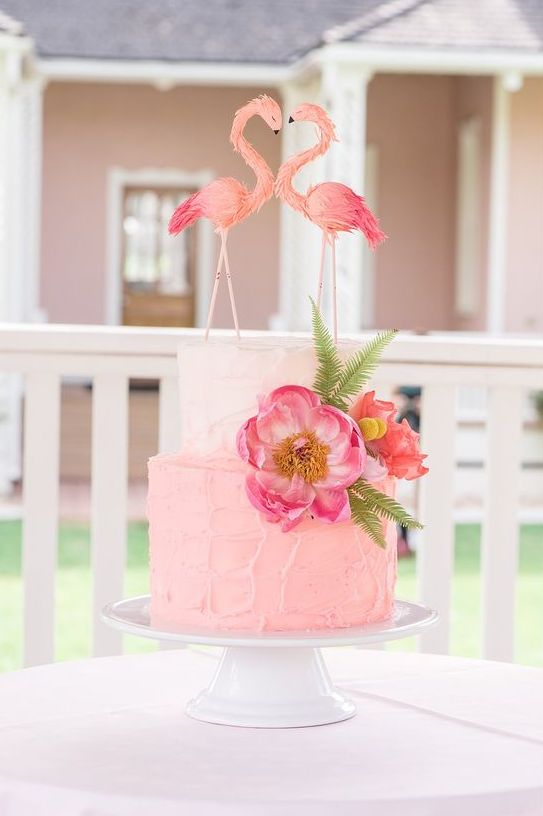 a textural pink wedding cake with hot pink and coral blooms and greenery and textural flamingo wedding cake toppers