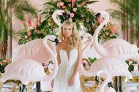 a tropical wedding arch with greenery and pink blooms and with blush flamingoes around is a creative and fun idea to rock