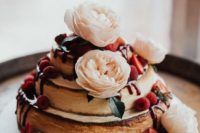 a two-stacked cheesecake topped with flowers and berries looks cute and rustic