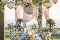 a very refined outdoor wedding reception with greenery and glam round crystal chandeliers hanging over the table