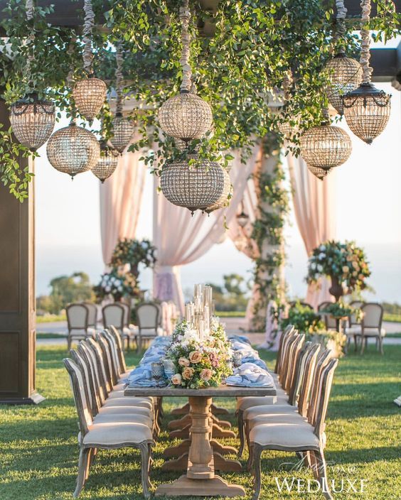a very refined outdoor wedding reception with greenery and glam round crystal chandeliers hanging over the table