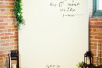 a wedding backdrop with a quote, greenery, candle lanterns and greenery is a cool and catchy indoor wedding decor idea