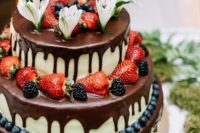 a wedding cheesecake with fresh blueberries, strawberries, blackberries chocolate drip, fresh blooms and a topper