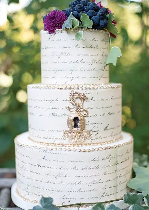 a whimsical wedding cake that features a whole text and some blooms and grapes on top is a gorgeous idea for a book-lover wedding