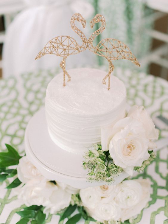 a white textural wedding cake topped with gold glitter geometric flamingos is amazign and very glam-like