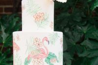 a white wedding cake paitned with greenery, blooms and flamingoes and with a tropical bloom on top is a gorgeous idea