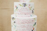 a white wedding cake with quotes, with small colorful painted blooms and a matching cake topper is pure fun for a summer wedding