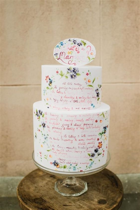 a white wedding cake with quotes, with small colorful painted blooms and a matching cake topper is pure fun for a summer wedding