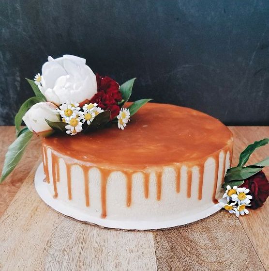 an earl grey cheesecake with salty dark caramel is topped with white peonies, green mist, red carnations, and chamomile flowers