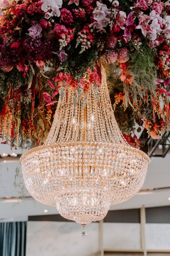 fantastic wedding decor - an oversized glam crystal chandelier surrounded with super bold and lush florals and greenery is wow