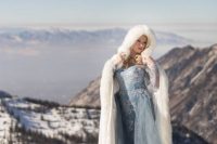 Elsa-inspired bridal look with a blue embellished wedding dress with long sleeves and an illusion neckline plus a faux fur coverup with a hood