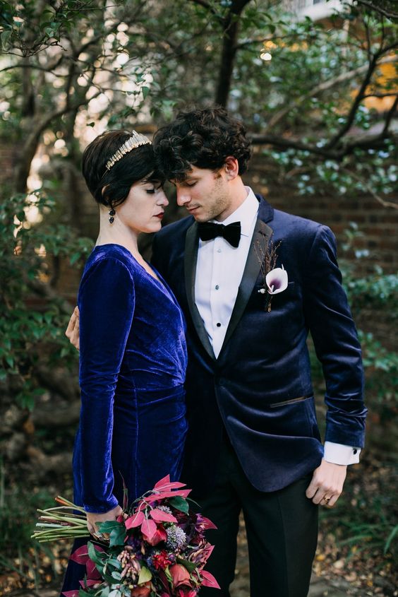 a Goth-inspired groom's look with a midnight blue velvet tux with black lapels, a black bow tie and pants and a calla boutonniere