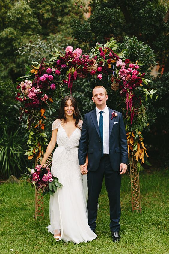 a bold floral wedding arch with plenty of greenery, pink, marsala and red blooms and magnolia leaves is veyr catchy