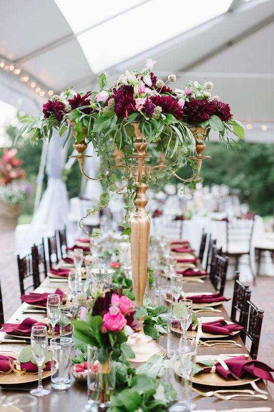 a bold summer wedding tablescape with gold chargers, candelabras with marsala blooms and pink ones plus marsala napkins