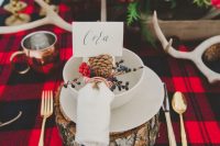a bold winter rustic wedding tablescape with stumps, a red plaid tablecloth, red and white blooms and antlers