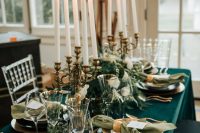a chic emerald wedding tablescape with emerald and green textiles, gold cutlery and candleholders, greenery on the table and tall and thin candles