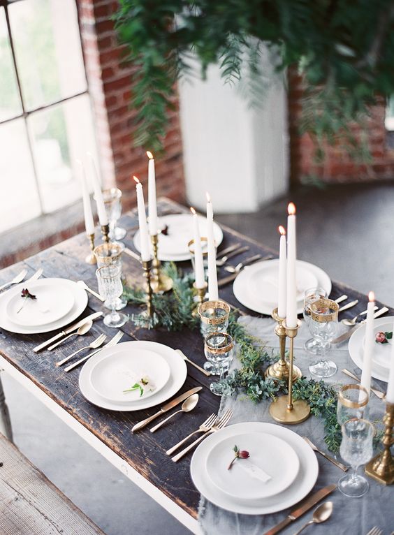 a chic tablescape with an evergreen table runner, gilded candle holders and gold rim glasses