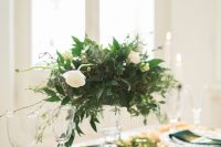 a chic wedding tablescape with navy napkins and ribbons, a greenery and white bloom centerpiece, moss and a gold table runner