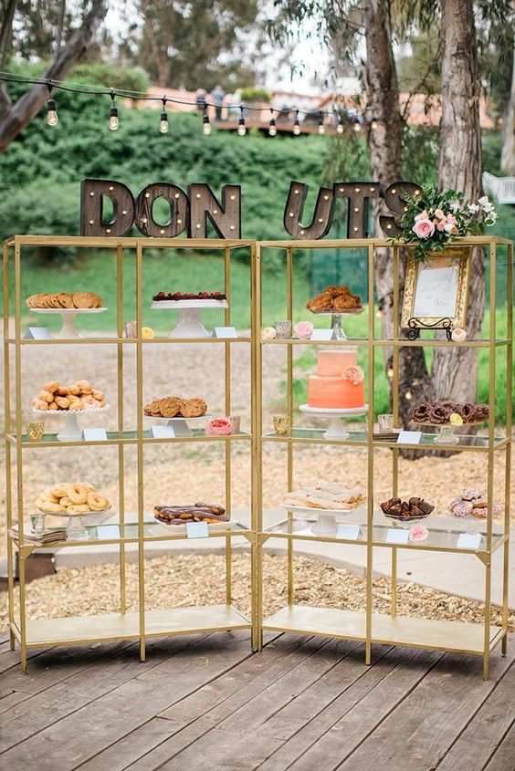 a cool wedding dessert display composed of two gilded shelves, decorated with marquee letters and blooms on top