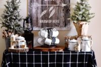 a cozy hot cocoa bar with snowy trees, wood slices, tin mugs and a cute sign over it