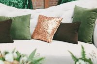 a cozy wedding lounge with emerald and gold sequin pillows, a green glass vase and ferns