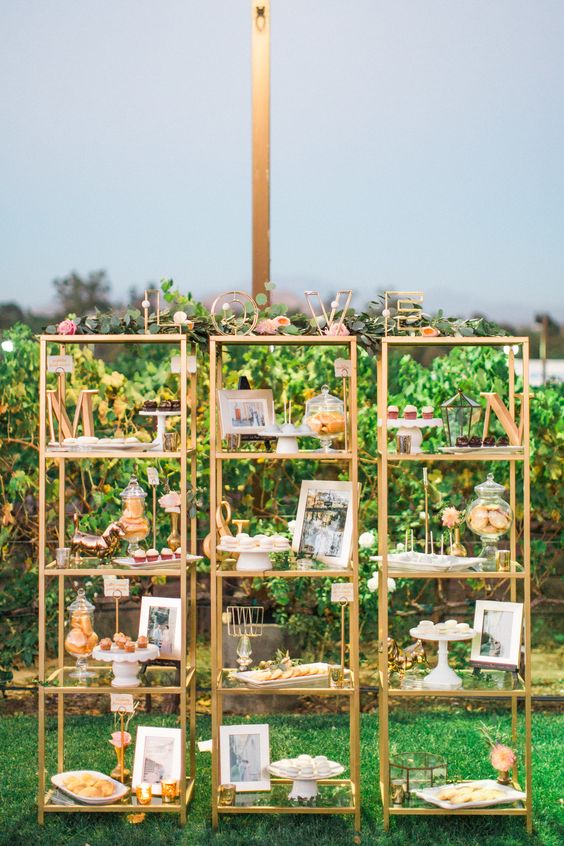 a creative and smart wedding dessert table composed of three gilded shelves, monograms and blooms