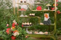 a creative gilded shelf as a wedding dessert stand, decorated with greenery and bright blooms