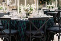 a dark tartan tablecloth paired with white blooms and greenery and with white candles for a refined wedding reception