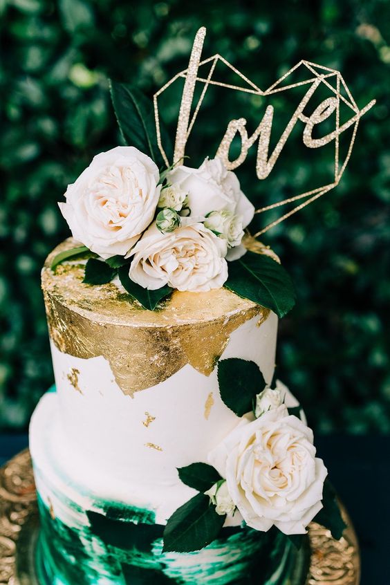 a fab wedding cake with a white and gold leaf and emerald brushstroke tier, neutral blooms, foliage, a gold glitter cake topper