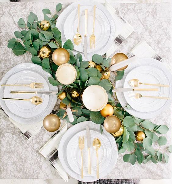 a glam tablescape with a foliage table runner, gold ornaments and cutlery plus goblets looks very festive-like