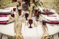 a glam winter tablescape with a gold sequin runner, neutral blooms, gold candleholders, marsala napkins and apples