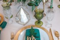 a gold charger and cutlery, green candles and a lush greenery centerpiece, emerald napkins