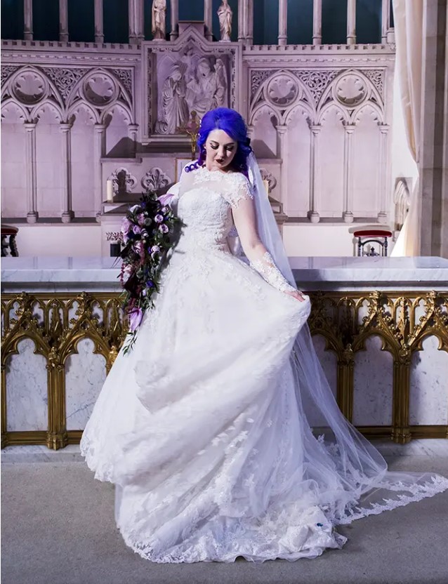 a gorgeous lace princess-style wedding gown with illusion sleeves and a neckline, a tain, purple hair and a dramatic bouquet
