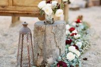 a greenery, white and burgundy bloom garland and a matching floral arrangement plus a candle lantern for accenting a winter wedding aisle