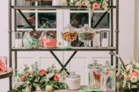 a large rustic shelving unit with greenery, white and pink blooms, signs and lots of candies is a lovely idea for a rustic wedding